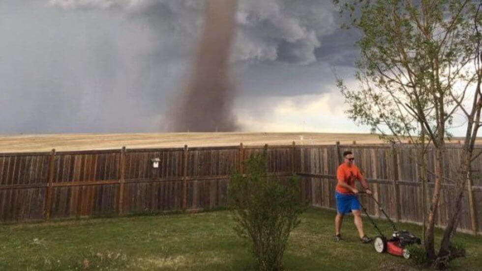 صورة شخص يجز العشب وخلفه إعصار